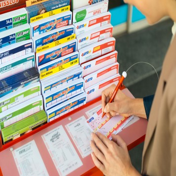 Una donna è in piedi vicino a un espositore schedine e compila una schedina Swiss Lotto. 